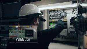 Industrial worker wearing META-aivi AR smart glasses inspecting an electrical control panel with AI-powered validation overlays, including error detection and real-time verification.
