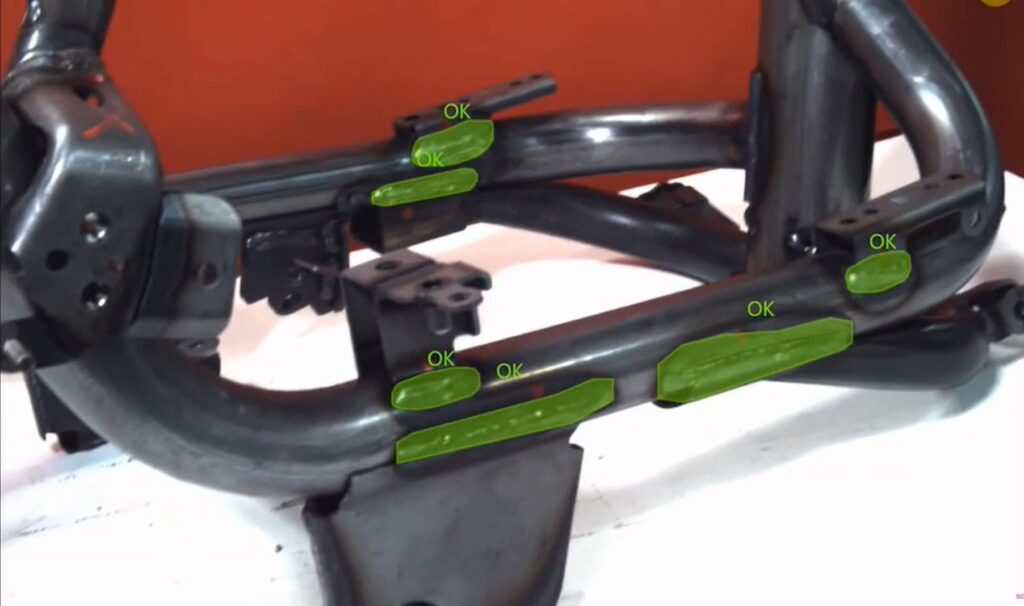 An industrial metal frame assembly undergoing welding inspection. The AR interface overlays green segmentation masks and "OK" labels onto verified weld joints, demonstrating how AI-powered defect detection supports human-AI collaboration and improves inspection accuracy in smart manufacturing.