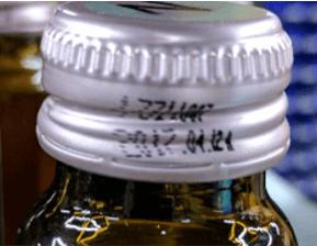 Example of skewed or distorted printed characters on bottle caps illustrating OCR readability issues.